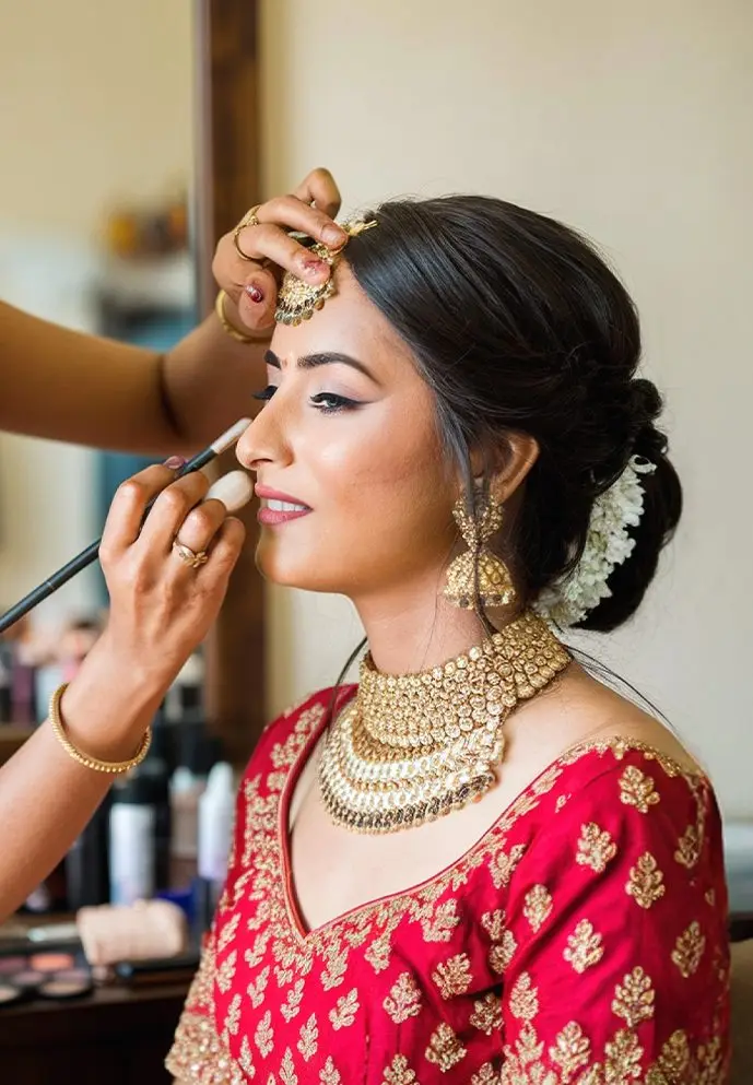 Bride in red having her makeup finished by an artist