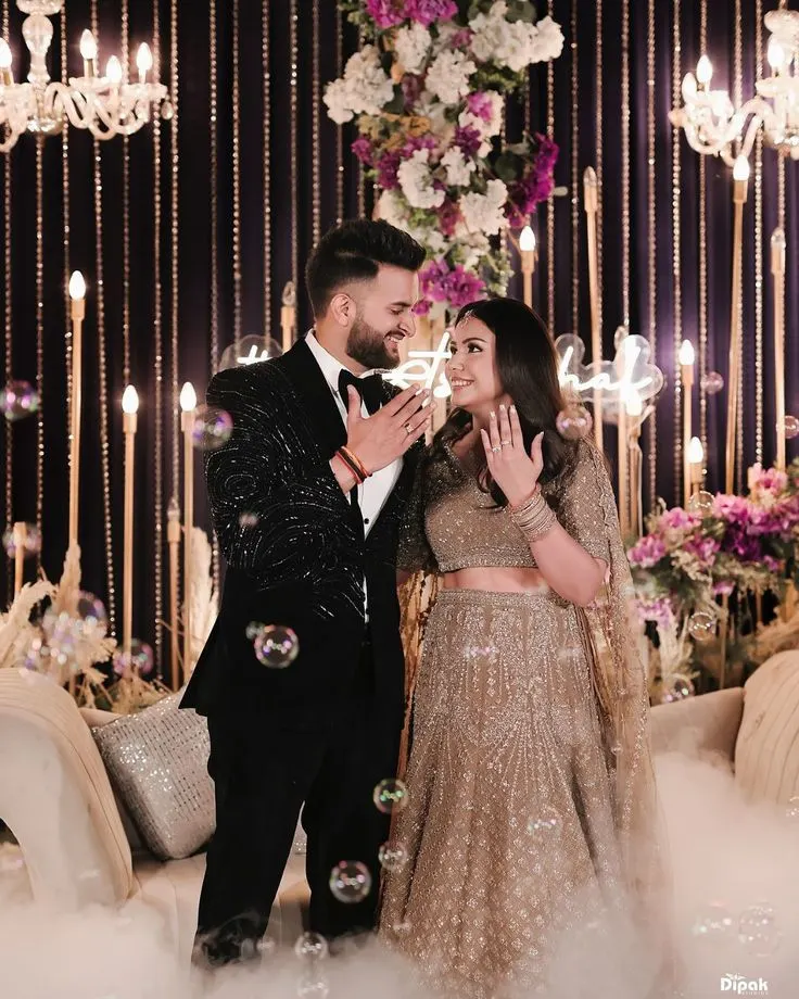 Engaged couple laughing in front of a floral and candlelit backdrop