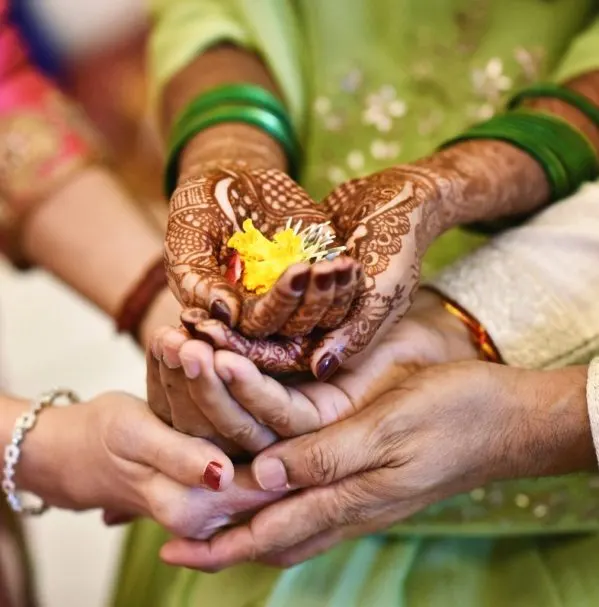 Hennaed hands cupping a marigold, held by family at the haldi