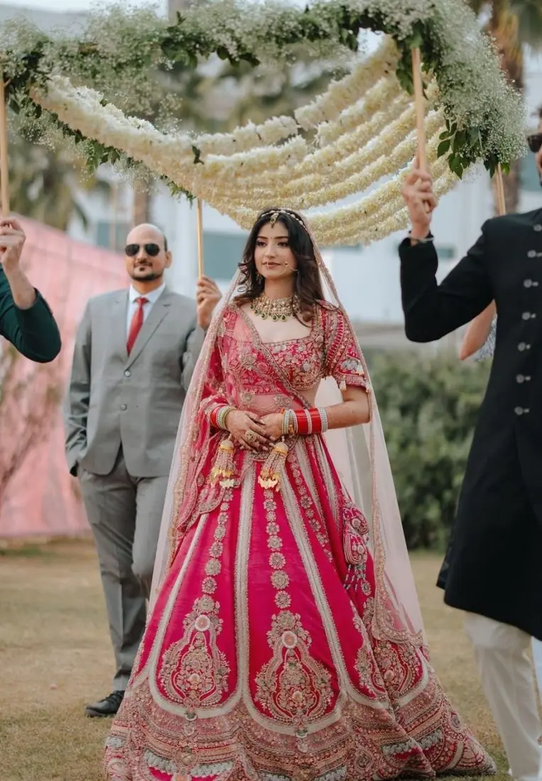 Bride in a pink lehenga walking under a floral chadar
