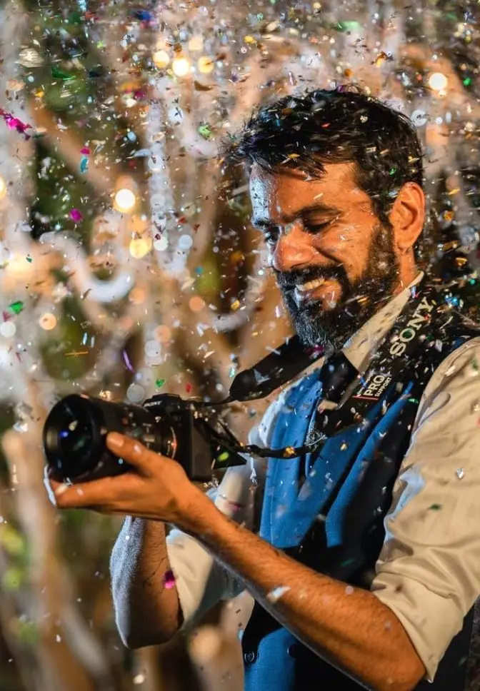 Wedding photographer smiling behind his camera amid confetti