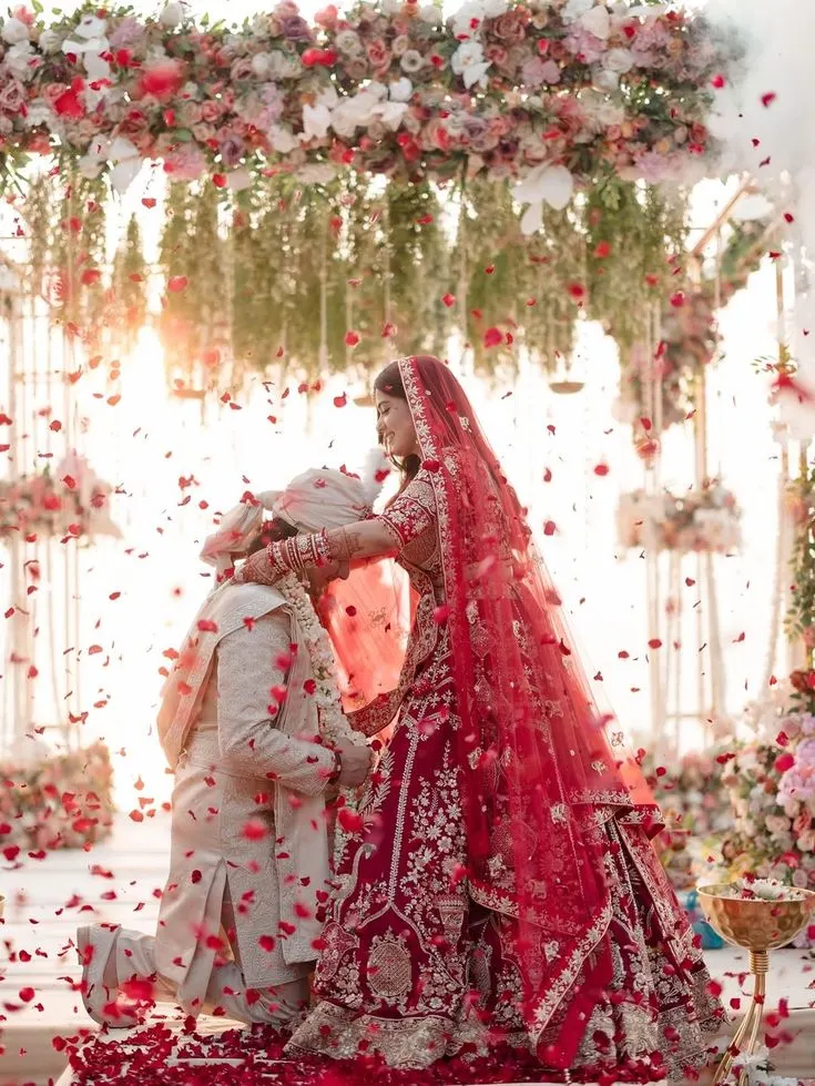 Bride placing the varmala on her groom as rose petals fall