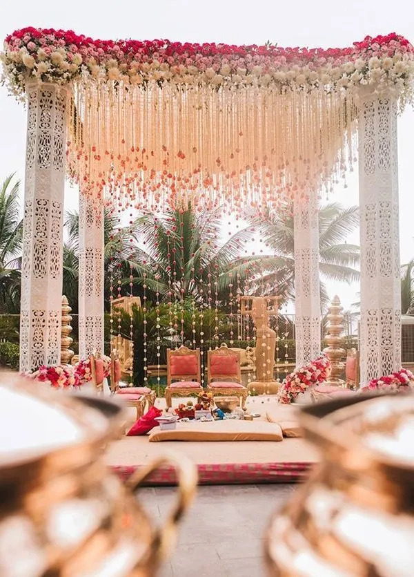 Carved white mandap with hanging floral strings among palm trees